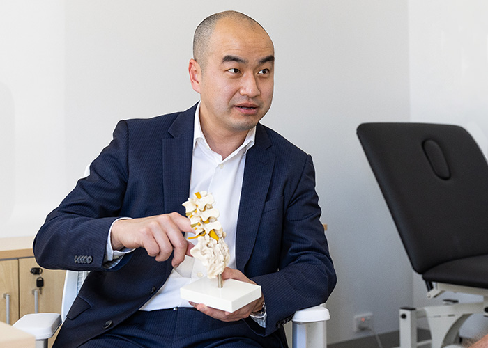 orthopaedic surgeon keat ooi is holding a model spine to demonstrate anatomy to a patient